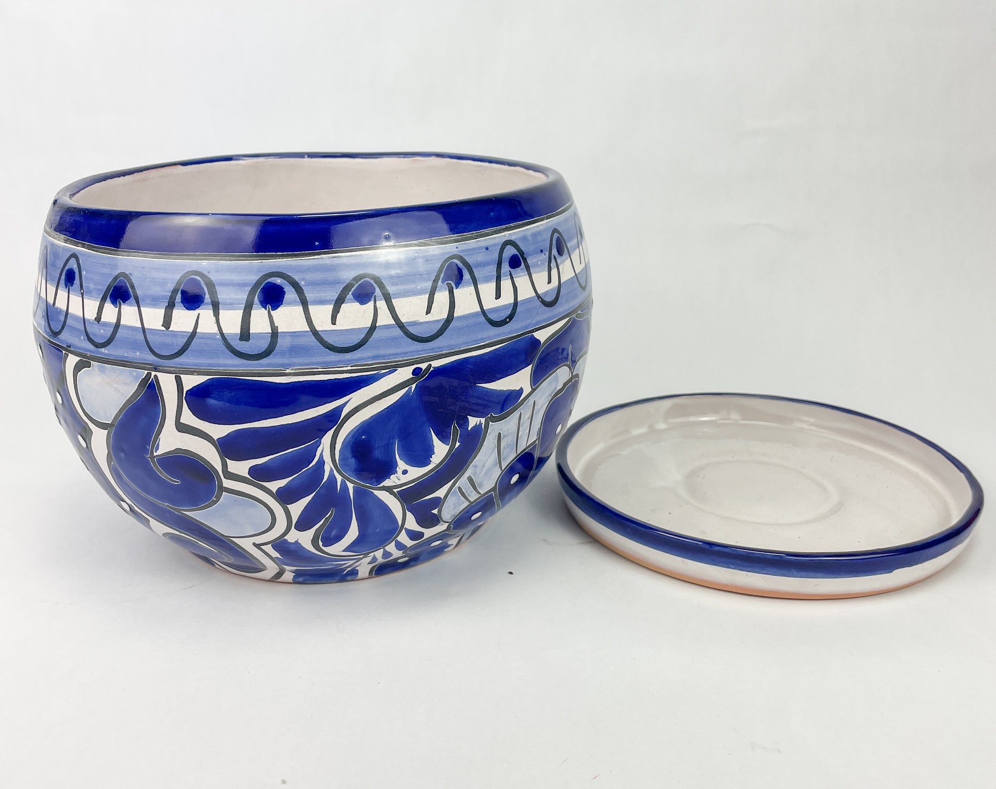 Hand-painted Talavera flower pot featuring vibrant floral design, part of authentic Mexican pottery collection. Talavera planters showcase traditional folk art on rustic furniture. Talavera tile adorns walls alongside Talavera animals in rich colors