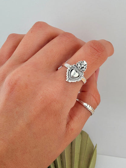 Close-up of hand wearing a Silver Sterling 925 Sacred Heart signet ring with detailed heart and flame design, styled with a simple silver band.
