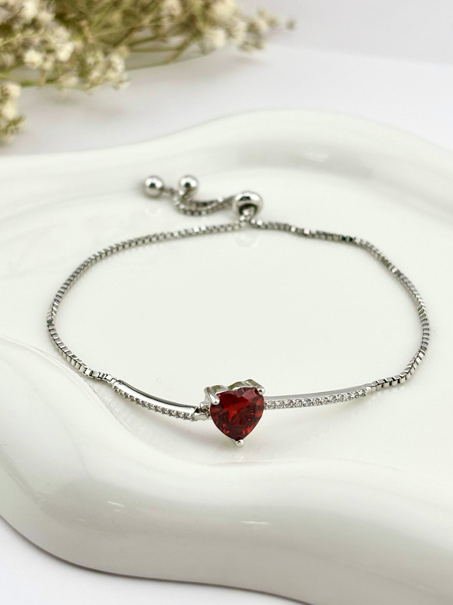 Silver Sterling 925 adjustable bolo bracelet with red CZ heart charm and delicate cubic zirconia accents displayed on a white jewelry dish.