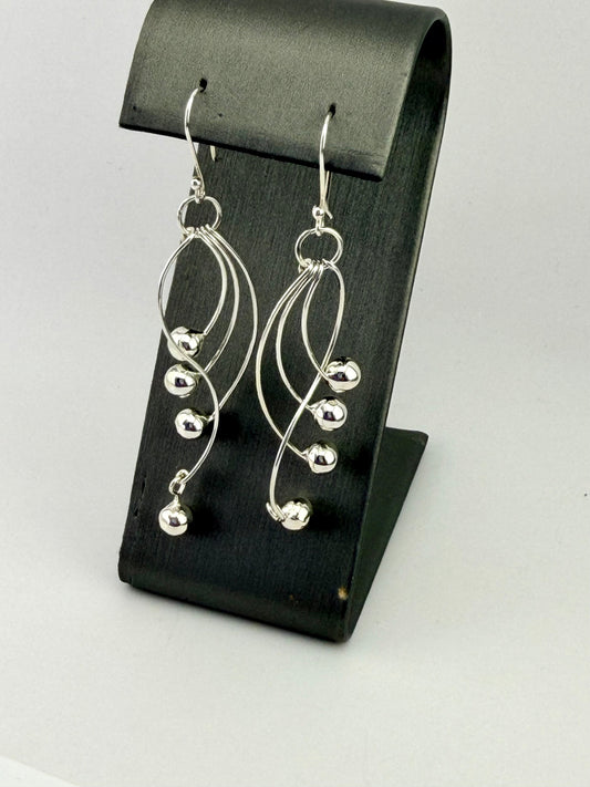 Sterling silver dangle earrings with curved wire design and polished silver bead accents displayed on a black jewelry stand.